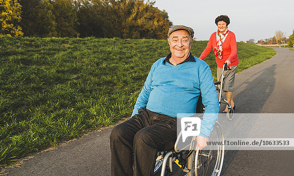 Lächelndes Seniorenpaar mit Rollstuhl und Rollator auf einem Weg