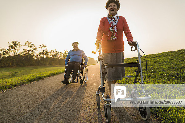 Smiling senior couple with wheelchair and wheeled walker on a path