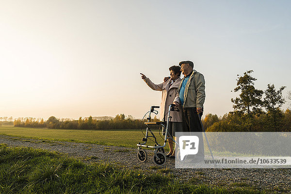 Senior couple with walking stick and wheeled walker standing in the nature