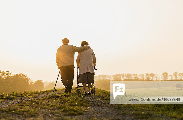 Senior couple walking with walking stick and wheeled walker in the nature