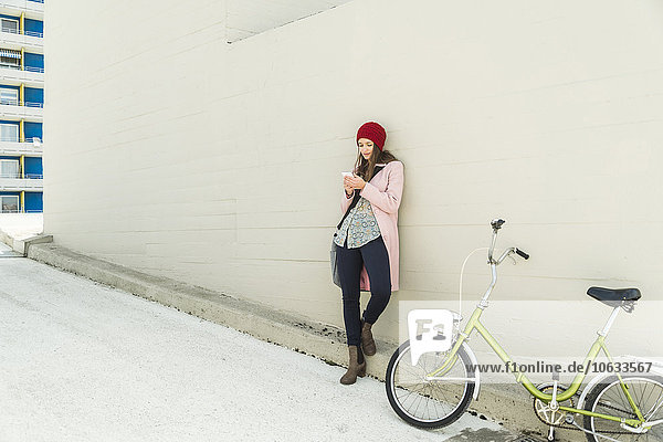 Junge Frau neben dem Fahrrad beim Blick aufs Handy
