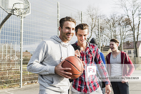 Young man with basketball and friends on basketball court