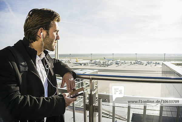 Germany  Frankfurt  Young businessman at the airport using smartphone with head phones