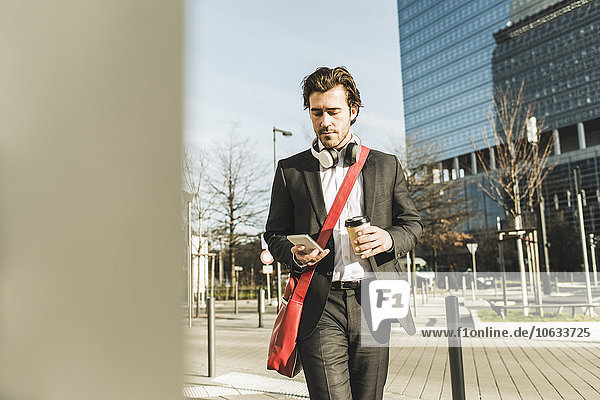 Deutschland  Frankfurt  Junge Geschäftsleute  die mit einer Tasse Kaffee durch die Stadt spazieren gehen  mit dem Handy