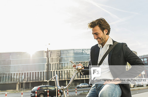 Germany  Frankfurt  Young businessman in the city with bicycle  using mobile phone