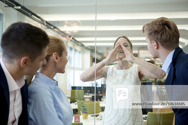 Businesswoman behind glass wall shouting at colleagues in office