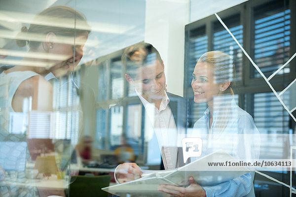 Smiling business team behind glass wall in office looking at folder