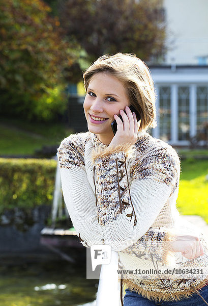 Austria  Mondsee  portrait of smiling young woman leaning on railing telephoning with smartphone