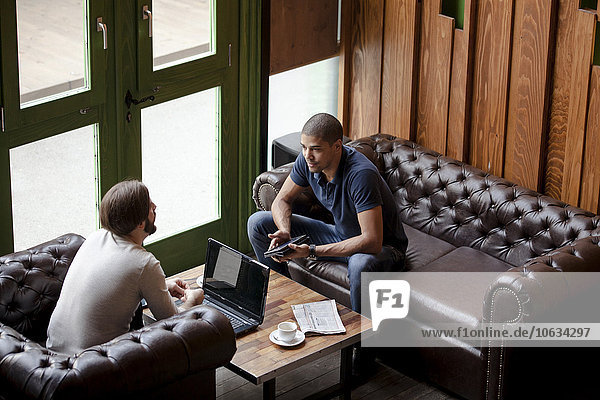 Two men with laptop sitting on couch in a lounge