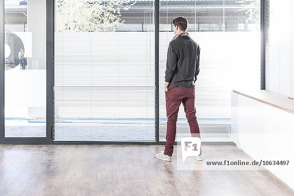 Man standing in empty office looking out of window