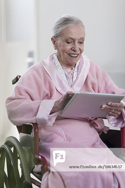 Smiling elderly patient in wheelchair using digital tablet
