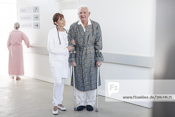 Arzt leitet ältere Patienten mit Krücken auf dem Krankenhausboden