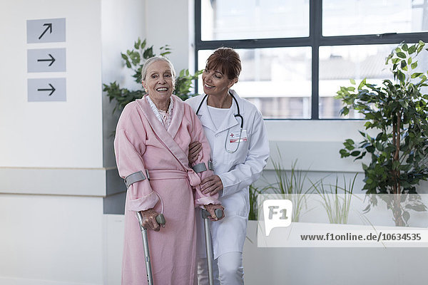Arzt leitet ältere Patienten mit Krücken auf dem Krankenhausboden