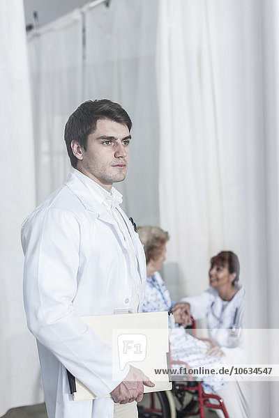 Serious doctor holding file with doctor and patient in background