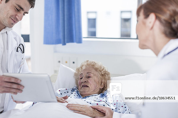 Doctor showing digital tablet to elderly patient in hospital bed