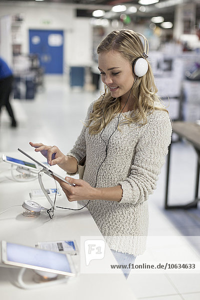 Junge Frau mit Kopfhörer testet digitales Tablett in einem Geschäft