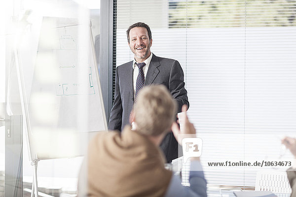 Laughing businessman at flip chart talking to colleagues
