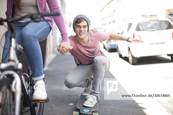 Teenage girl on bicycle pushing young man on skateboard