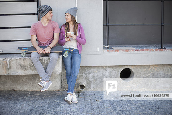 Junger Mann mit Skateboard und Teenagermädchen im Freien sitzend