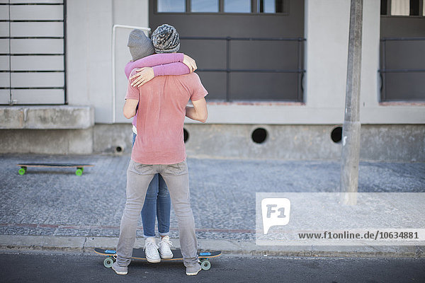 Junges Paar mit Skateboardumarmung auf der Straße