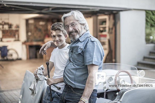 Porträt von Großvater und Enkel beim gemeinsamen Restaurieren eines Autos
