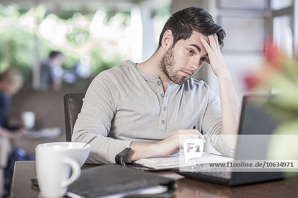 Frustrierter Mann sitzt am Esstisch und arbeitet zu Hause.