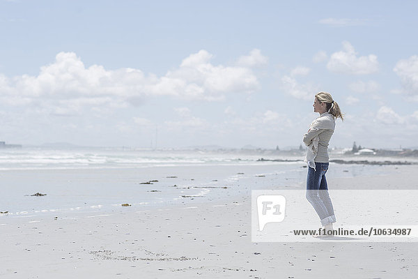 Frau steht am Strand und schaut in die Ferne.