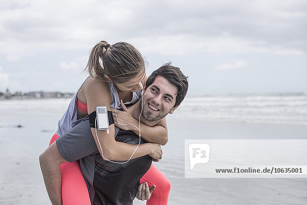 Young man carrying girlfriend piggyback on beach