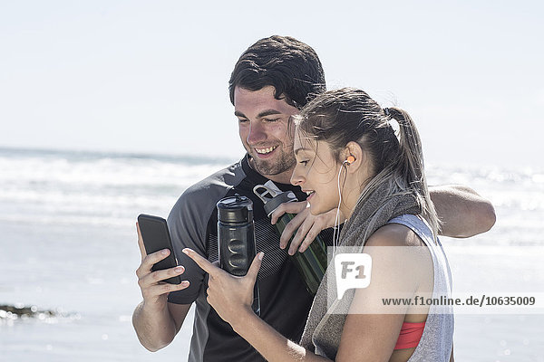 Sportive man and woman on beach looking at cell phone