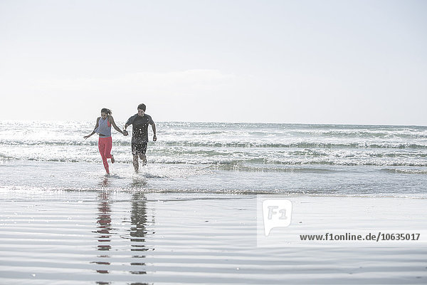 Junger Mann und Frau laufen Hand in Hand im Ozean