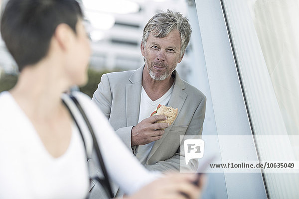 Ein reifer Mann isst ein Sandwich und redet mit einer jungen Frau.