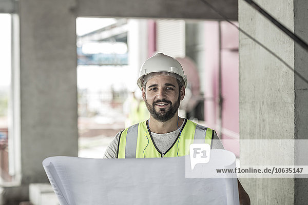 Porträt eines lächelnden Bauarbeiters mit Bauplan auf der Baustelle