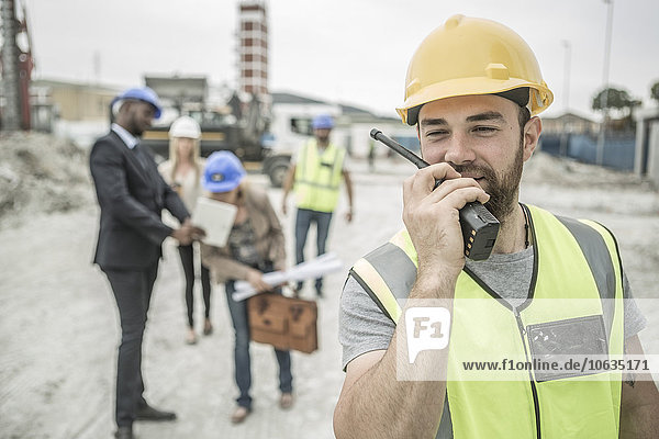 Construction worker with walkie-talkie on construction site with executives in background