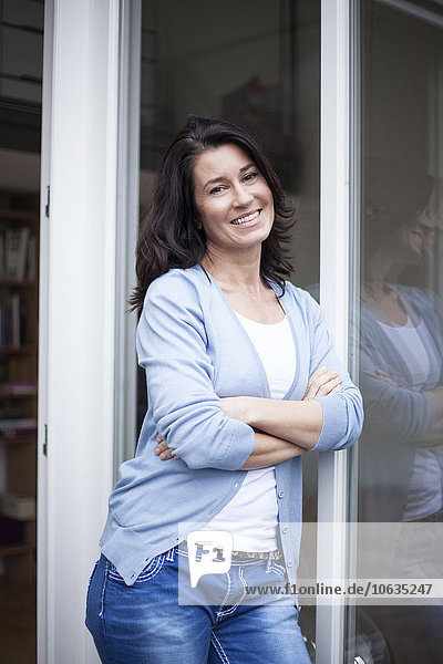 Portrait of smiling woman leaning against balcony door