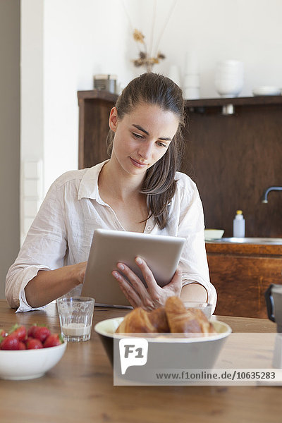 Young woman sitting at dining table using digital tablet