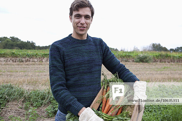 Man holding harvested carrots in field  portrait