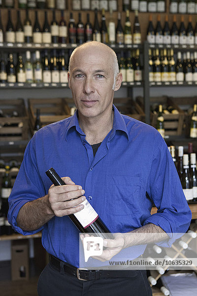 Mature man holding wine bottle in wine shop  portrait