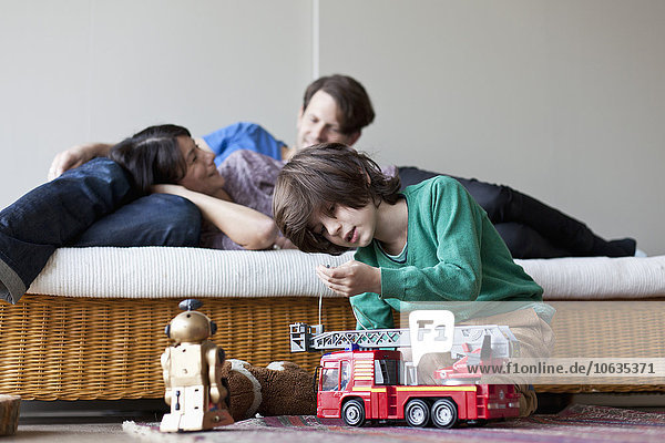 Junge spielt mit Spielzeug  Mutter und Vater liegen auf dem Sofa im Hintergrund