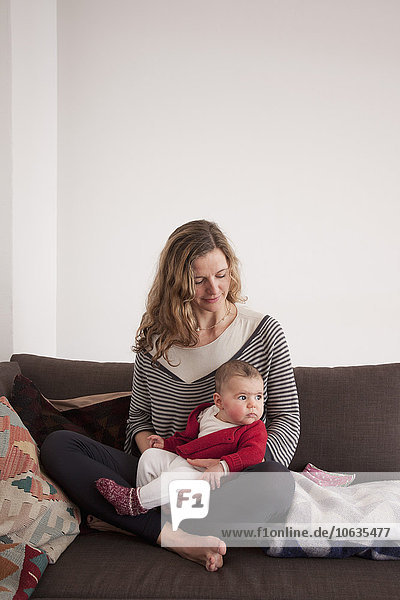 Woman sitting with baby girl on sofa at home