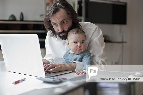 Mittlerer Erwachsener Mann  der am Laptop arbeitet  während er mit einem kleinen Mädchen zu Hause sitzt.