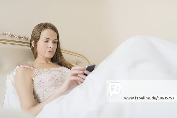 Junge Frau mit Smartphone im Bett zu Hause