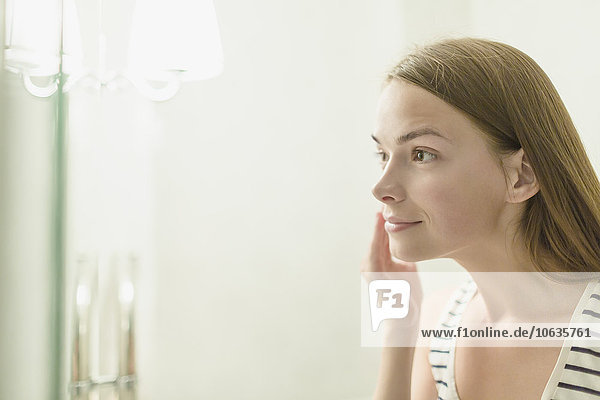 Beautiful woman applying cream on face in domestic bathroom
