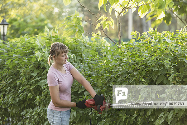 Frau schneidet Pflanzen mit Heckenschere auf dem Hof