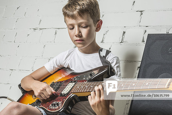 Junge spielt Gitarre  während er zu Hause sitzt.