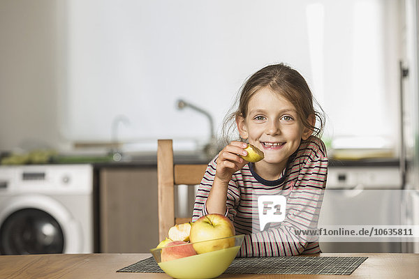 Porträt eines glücklichen Mädchens beim Apfelessen am Tisch