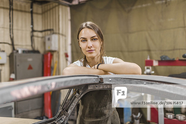 Porträt einer selbstbewussten Mechanikerin  die sich auf das Auto in der Garage stützt.