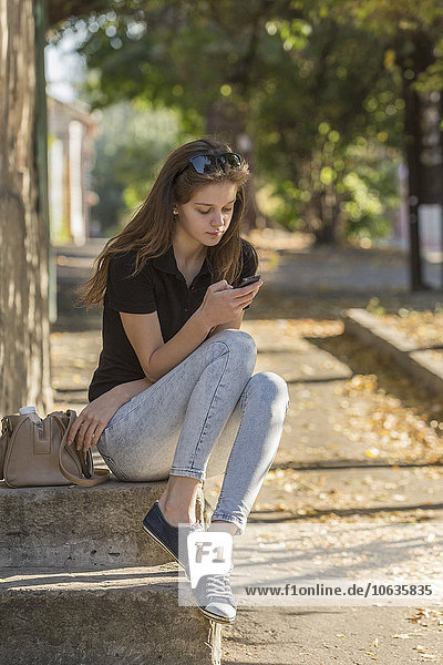 Woman using smart phone while sitting on steps outdoors