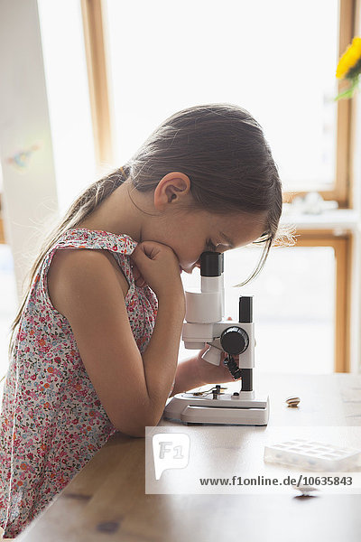 Side view of curious girl looking into microscope on table at home
