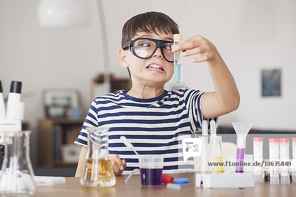 Ein kreuzäugiger Junge schaut auf das Reagenzglas während eines wissenschaftlichen Experiments im Haus.