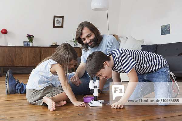 Happy family looking at boy using microscope on hardwood floor